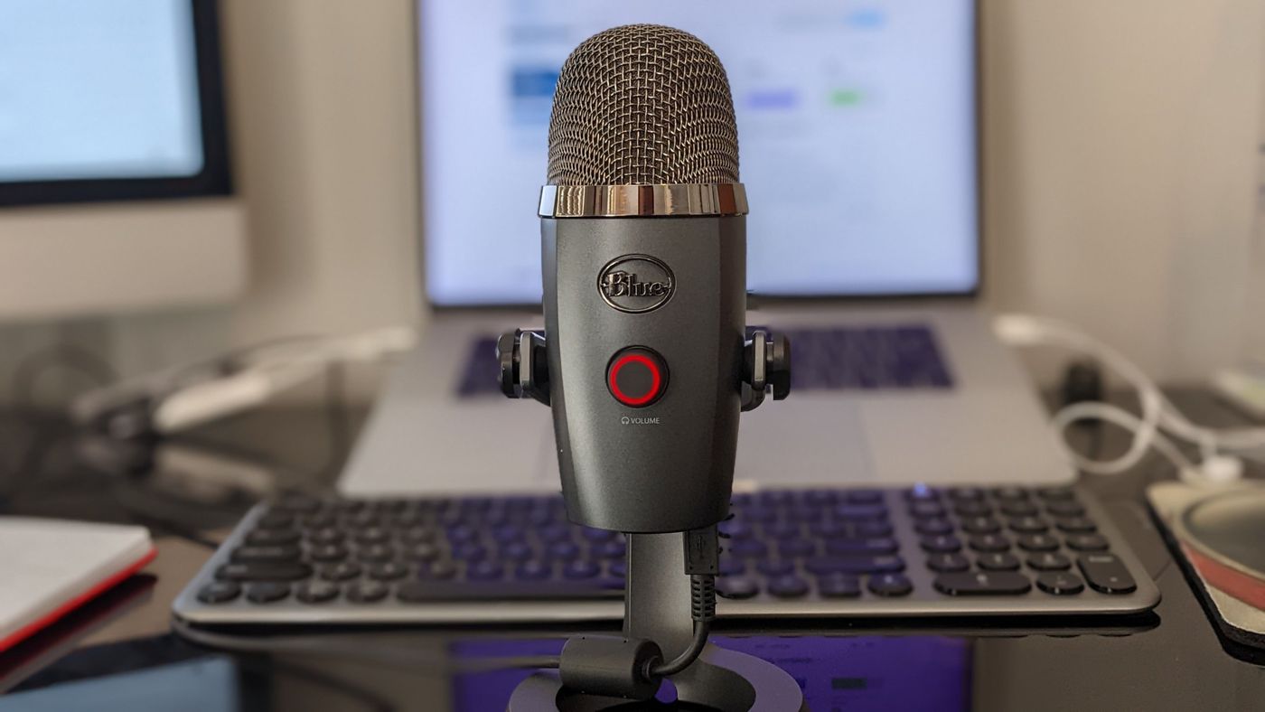 A USB microphone on a desk in front of a laptop
