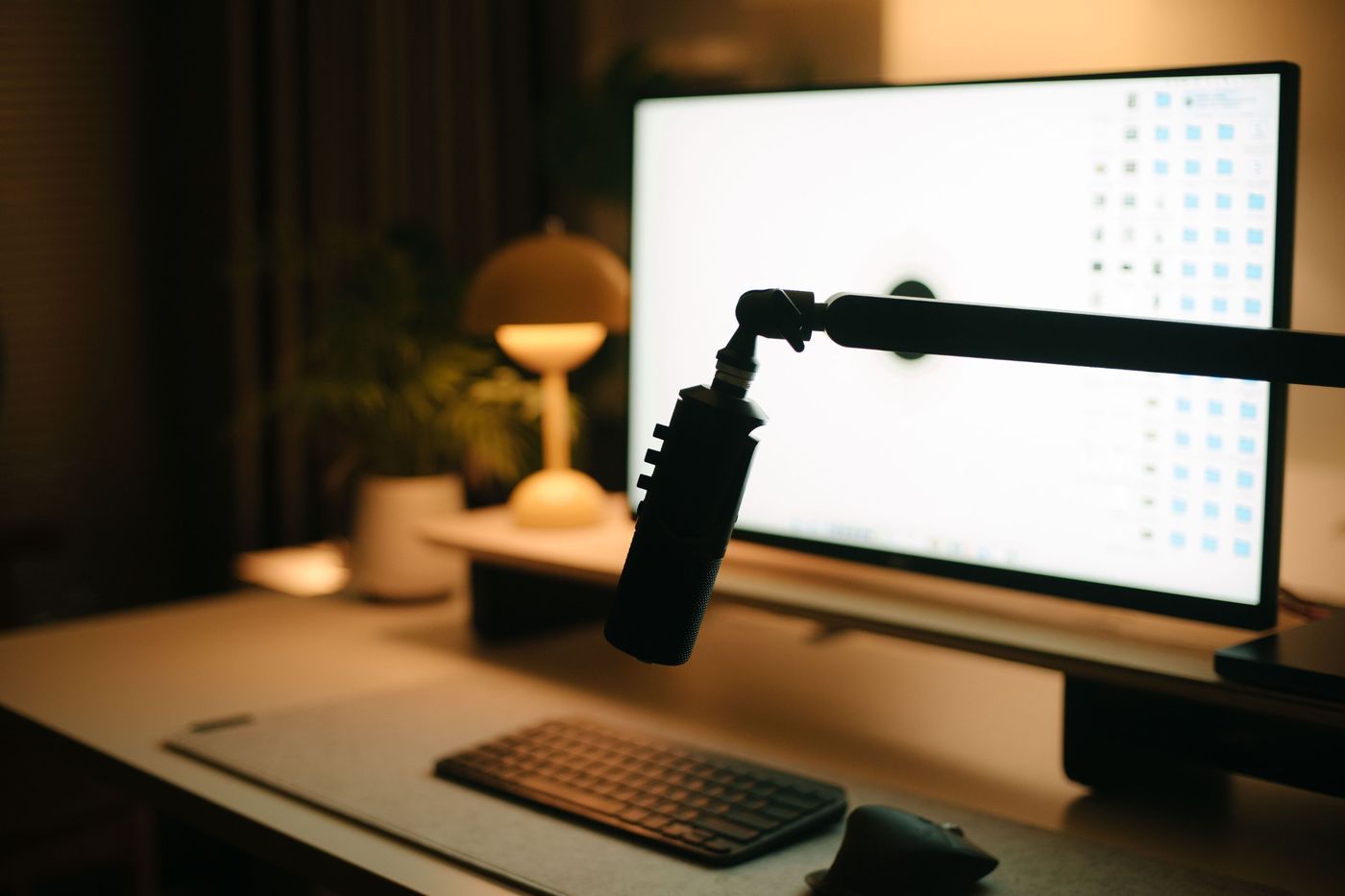 A boom-arm microphone in front of a monitor on a warmly lit desk