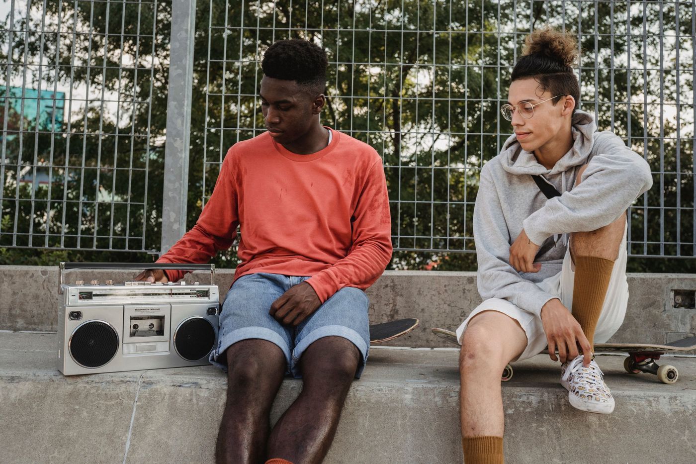 Two friends sitting on a wall with a boombox and a skateboard