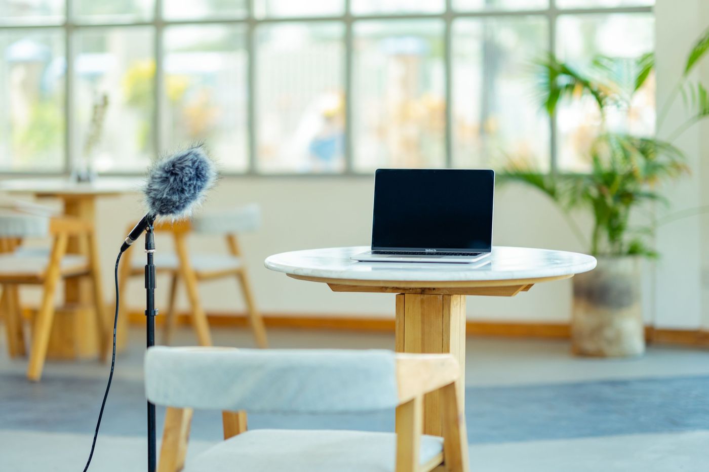 A microphone on a stand and a laptop on a table in a bright cafe