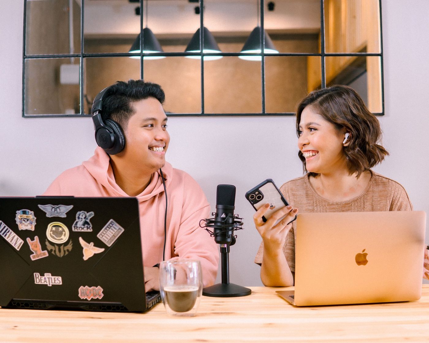 Two presenters laughing together at a table with a microphone and laptops