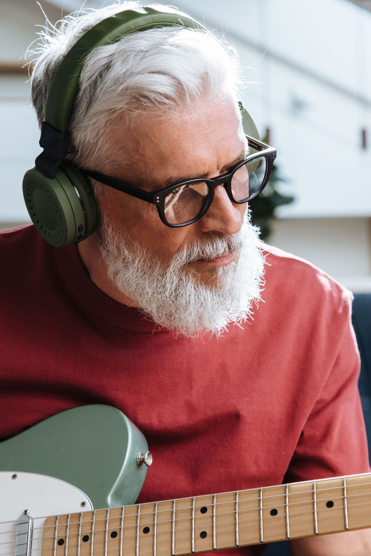 A man with a grey beard in green headphones playing an electric guitar
