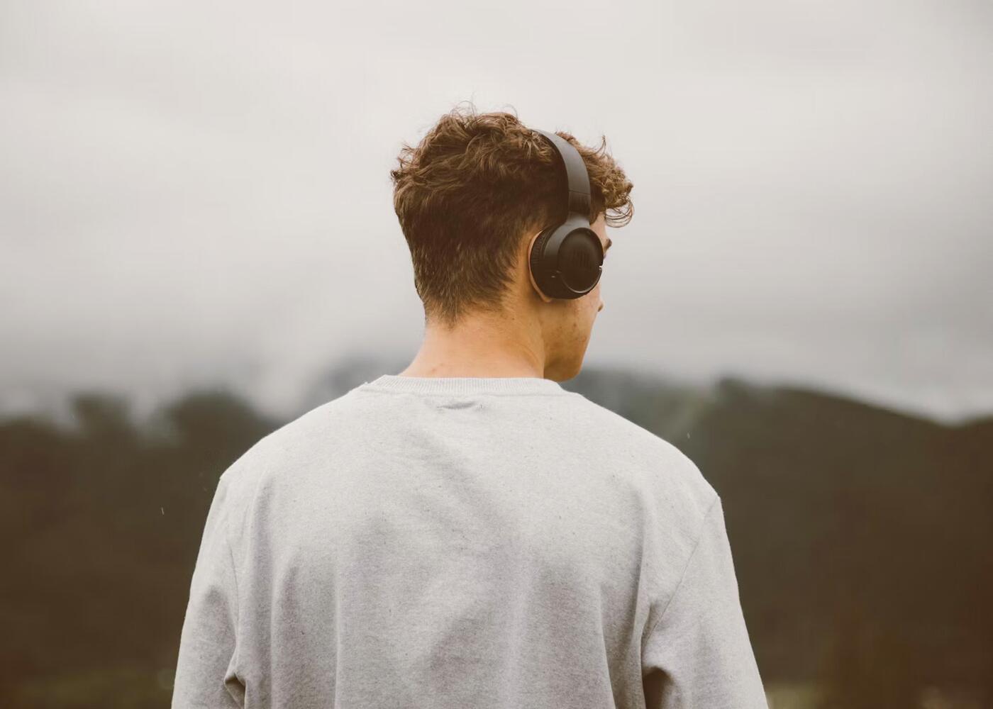 A young man in over-ear headphones listening outdoors