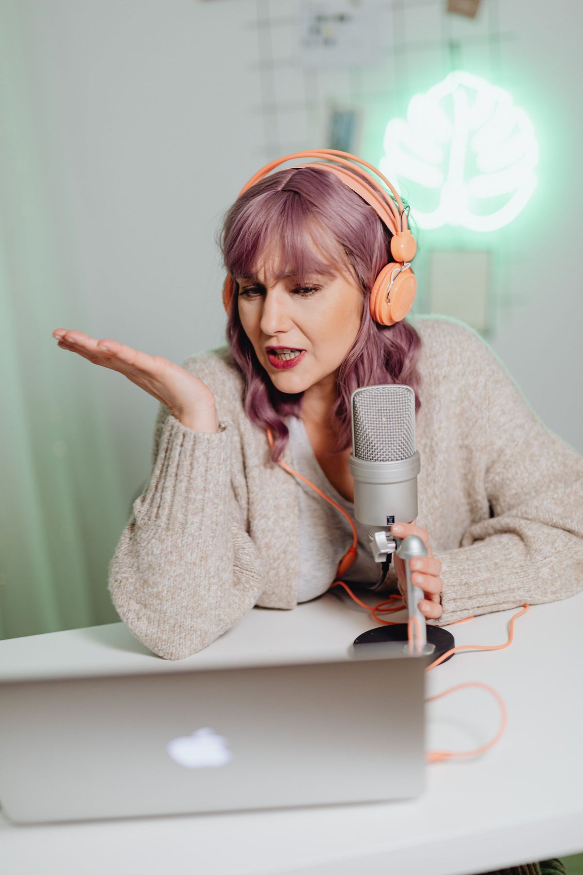 A presenter in orange headphones speaking into a microphone at a laptop