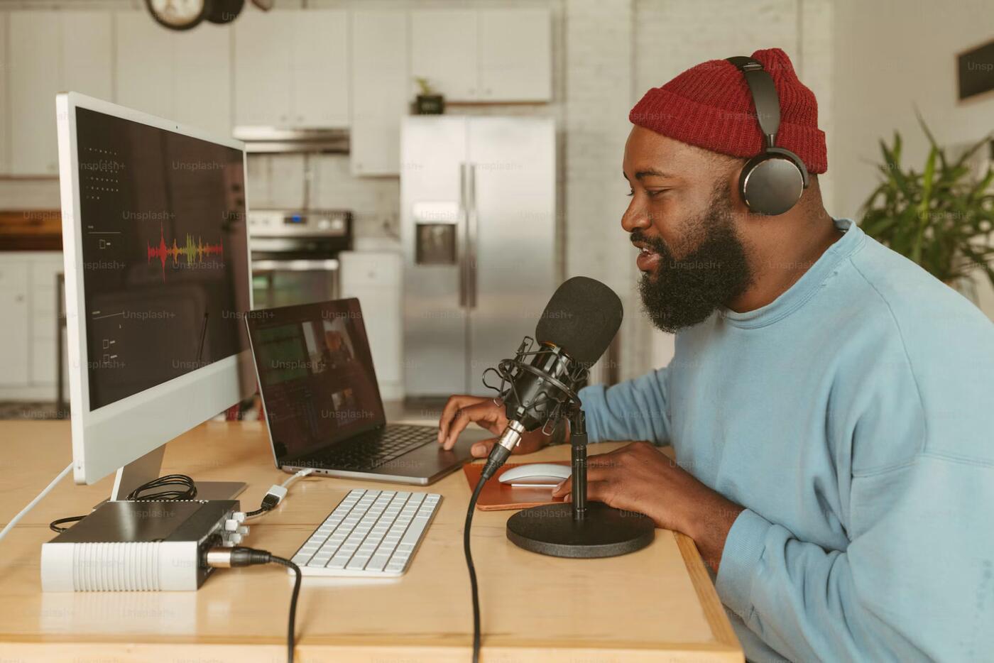 A broadcaster in headphones speaking into a studio microphone at his desk